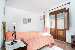 A bedroom with a bed, a nightstand, a lamp, a window with curtains, and a door.