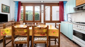 Een eethoek met een tafel en stoelen, een keuken met een fornuis, en uitzicht door een raam.