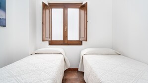 Een slaapkamer met twee bedden, een raam met houten luiken en een betegelde vloer.
