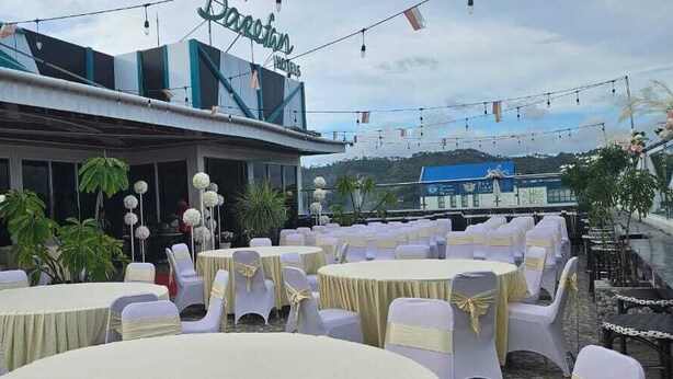 An outdoor banquet area with round tables and white chairs, decorated with white floral arrangements.