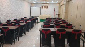 A conference room with rows of tables and chairs, each with a red bow. There is a whiteboard, a podium, and a flag on the wall.
