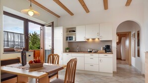 A modern kitchen with white cabinets, a dining table, and chairs. There is a window with a view of greenery outside. - Apartment 'Sonnblick' with Mountain View, Shared Garden and Wi-Fi (Laives)