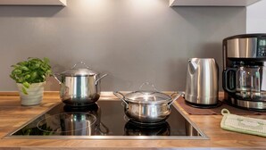 A kitchen with a stovetop, two pots, a kettle, a coffee maker, and a potted plant.