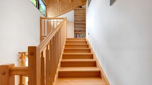 A wooden staircase with a handrail, leading to a landing with a white door and a shelf with books.