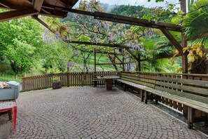 A covered outdoor area with a wooden bench, a stone table, and a wooden pergola with hanging purple flowers. - Apartment 'Waldruhe' with Mountain View, Shared Garden and Wi-Fi (Laives)