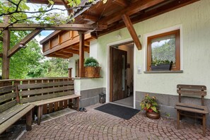 Eine Holzbank, eine Tür, ein Fenster mit einer Pflanze und ein Holzbau mit Dach.