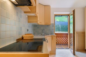 A modern kitchen with a large sink, wooden cabinets, and a view of a garden through an open door.
