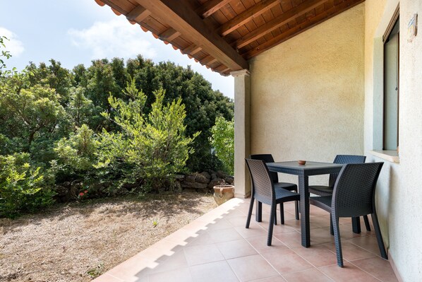 An outdoor patio with a table and chairs, surrounded by a garden and a stone wall.