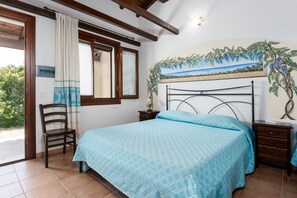 Um quarto com uma cama, uma cadeira, uma mesa de cabeceira, uma janela com cortinas e uma pintura na parede.