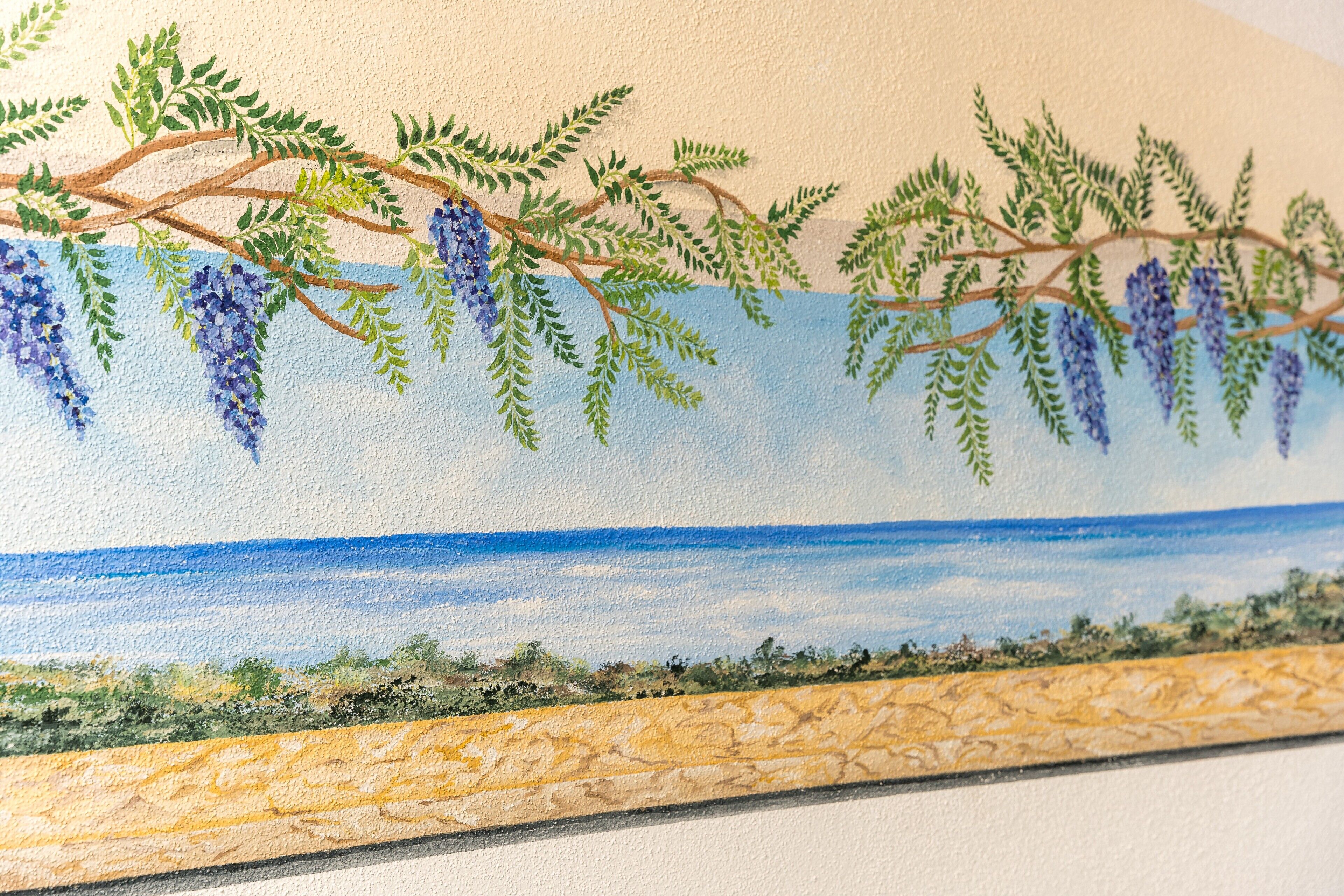 Un mur orné d’un paysage peint, représentant un arbre aux fleurs violettes pendantes et un ciel bleu.