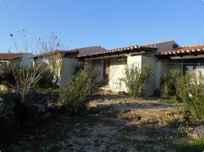 A residential building with a tiled roof, a front porch, and a garden with shrubs and a small tree.