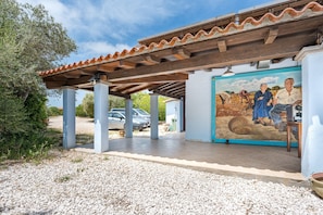Et overdækket udendørs område med et taglagstegl tag, et muralmaleri og en grussti.
