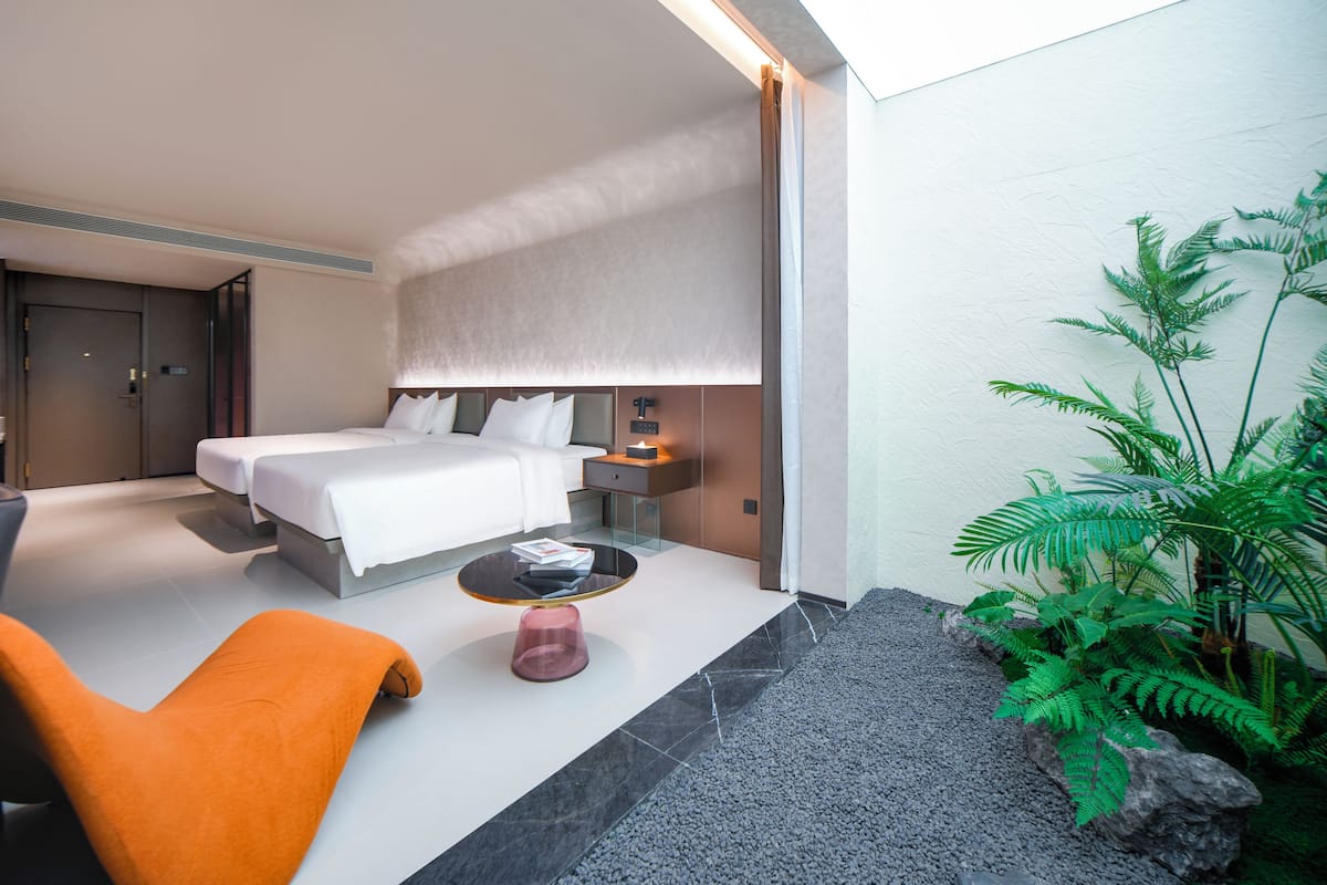 A modern hotel room with a large bed, bedside table, and a small seating area with a chair and table.
