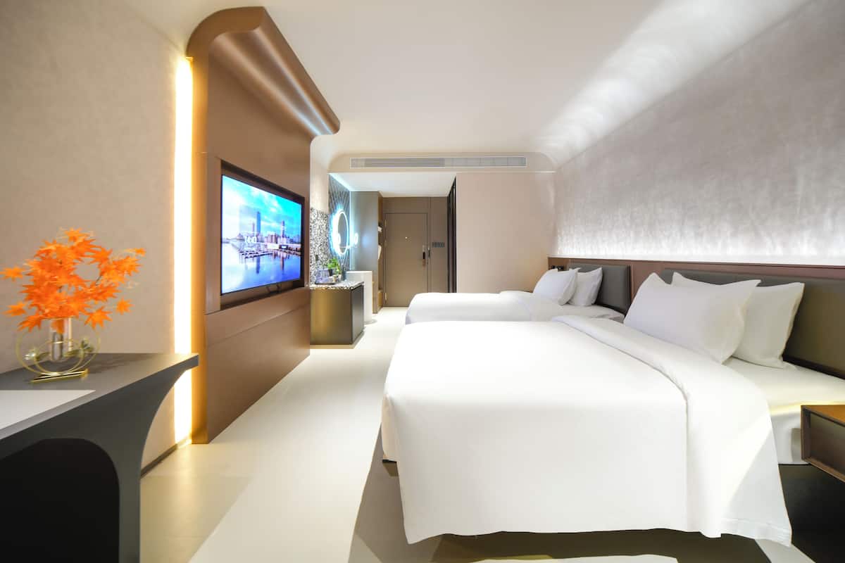 A modern hotel room with two beds, a TV, and a vase of flowers.
