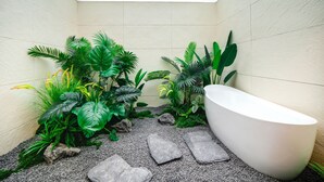 A bathroom with a bathtub, surrounded by tropical plants and a pebble floor. - chongqinglangxidujiajiudian (Deyang)