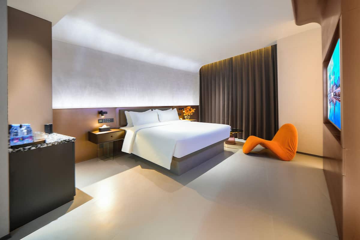 A modern hotel room with a large bed, a nightstand, a desk with a lamp, and a television.