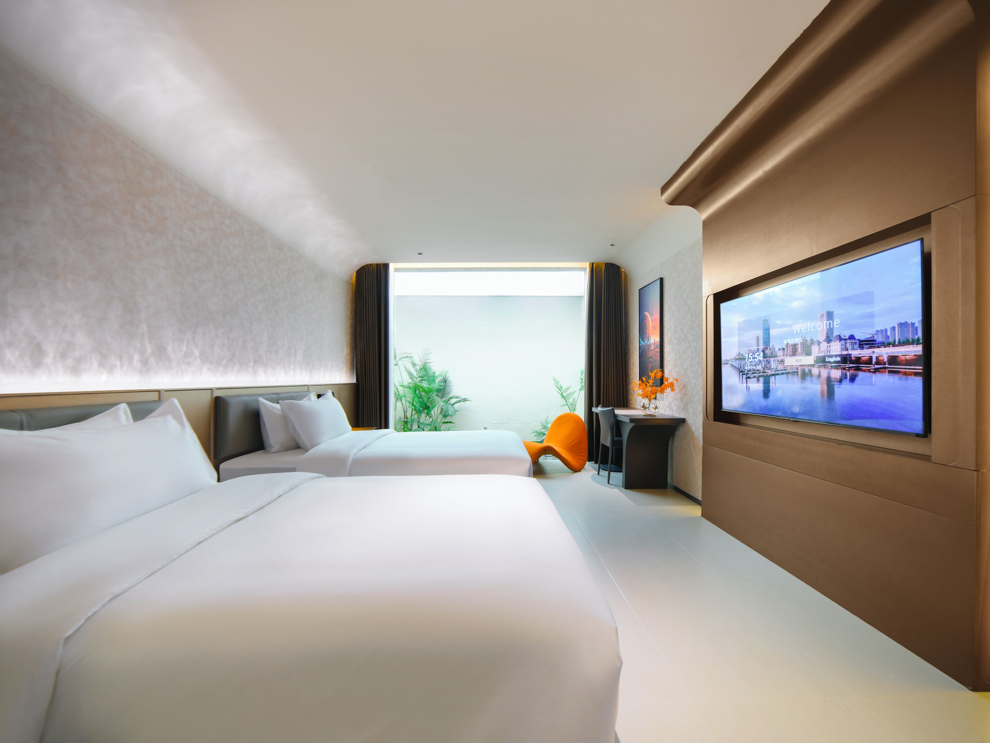 Een moderne hotelkamer met twee grote bedden, een bureau, een stoel en een groot televisiescherm waarop een stadsgezicht te zien is.
