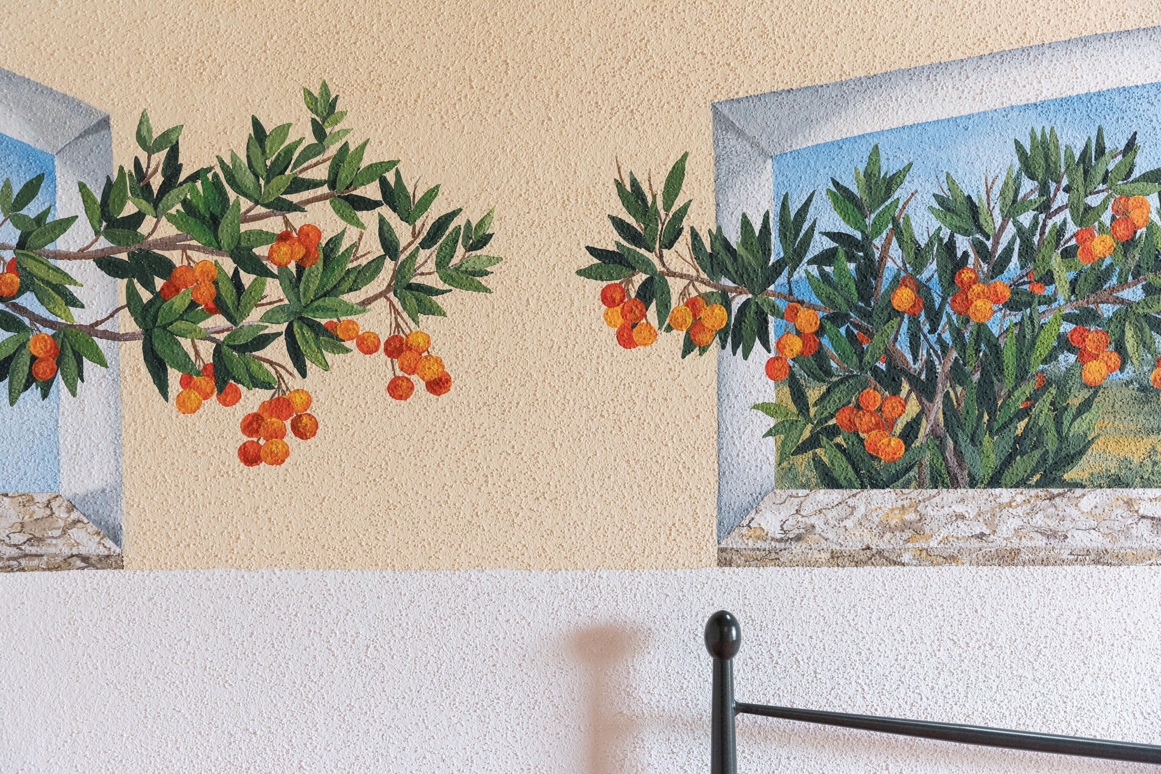 Een muur met een muurschildering van een plant met groene bladeren en oranje bessen.