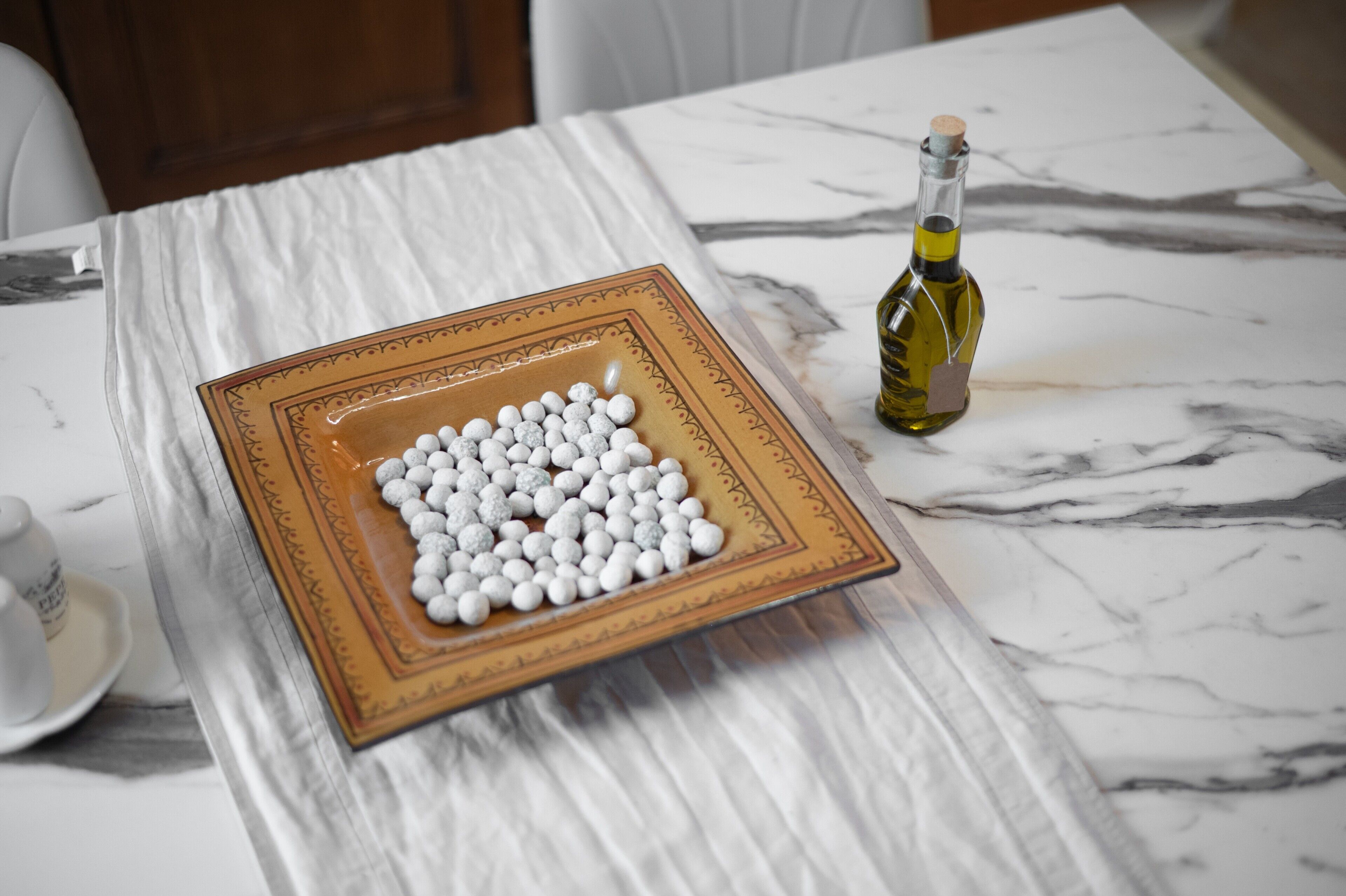 A marble table with a decorative plate of white spherical objects and a bottle of olive oil.