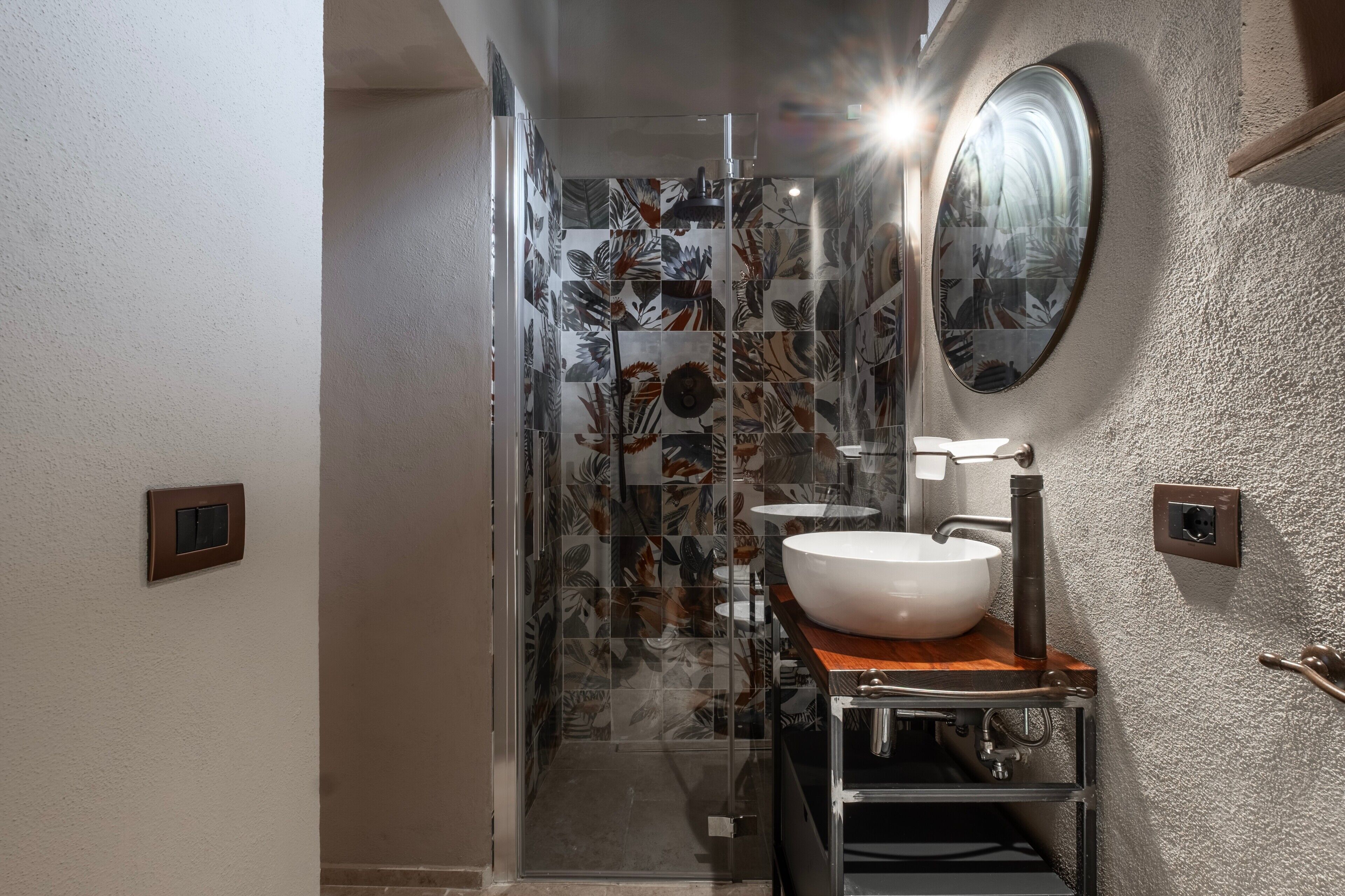 Ein Badezimmer mit Duschkabine aus Glas, einem weißen Waschbecken mit Holztischplatte und einem runden Spiegel an der Wand.