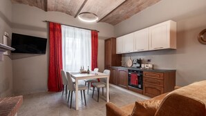A modern kitchen with white cabinets, a dining area with a table and chairs, and a TV mounted on the wall. - Apartment 'Il Rifugio Illuminato - Morellino' with Shared Garden, Wi-Fi and Air Conditioning (Semproniano)