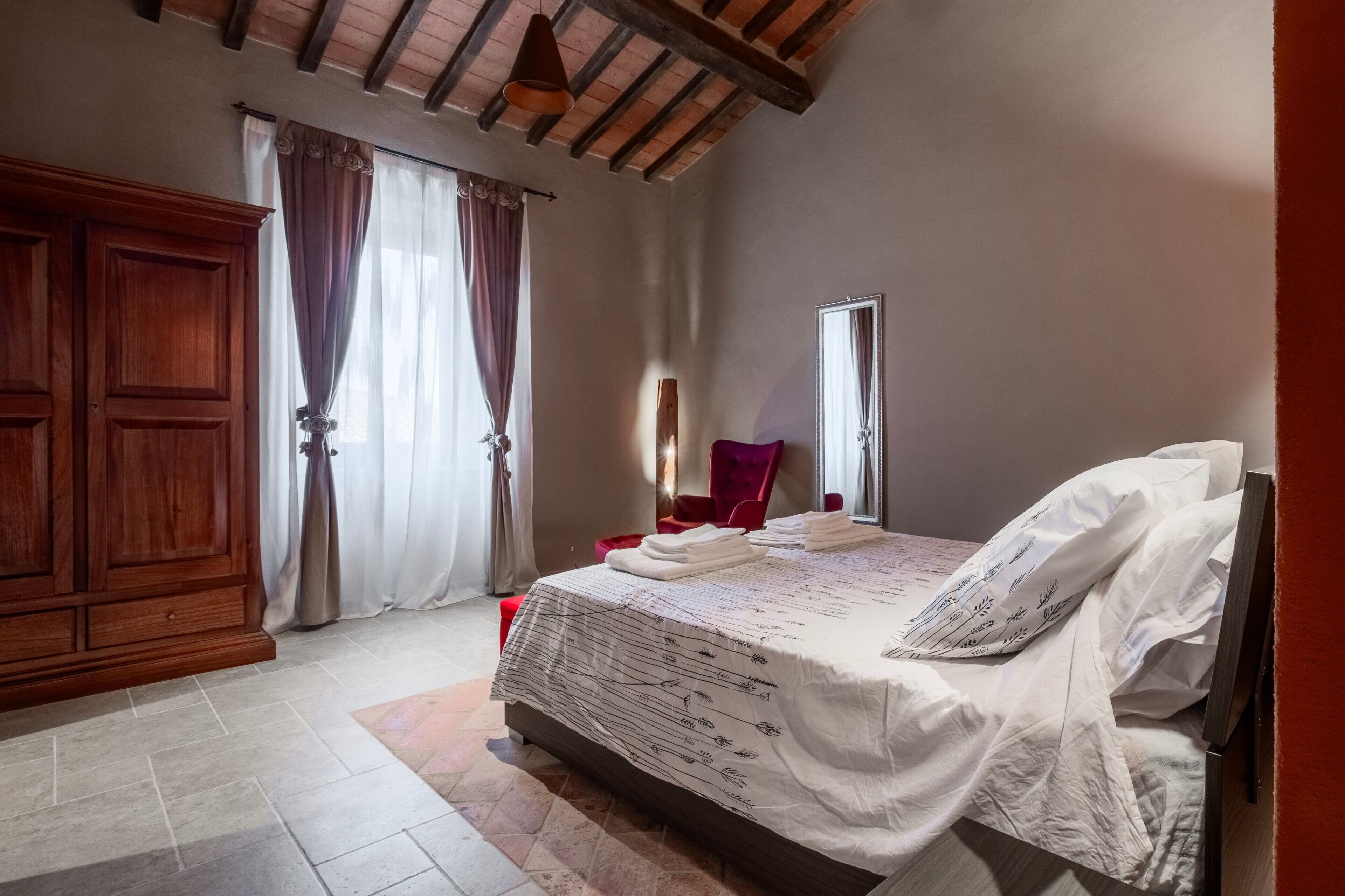 Un dormitorio con cama, armario de madera, cortinas y ventana.
