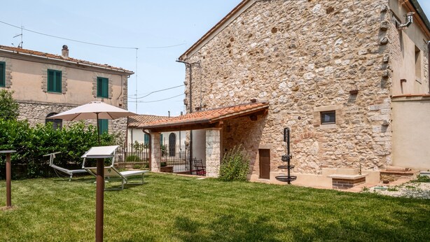 A stone building with a tiled roof, a covered patio, and a grassy yard. - Apartment 'Il Rifugio Illuminato - Brunello' with Shared Garden, Wi-Fi and Air Conditioning (Semproniano)