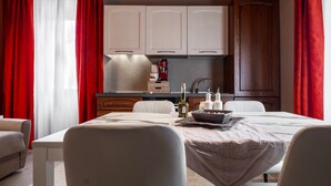A dining area with a table set for four, a kitchen with white cabinets, and red curtains. - Apartment 'Il Rifugio Illuminato - Brunello' with Shared Garden, Wi-Fi and Air Conditioning (Semproniano)