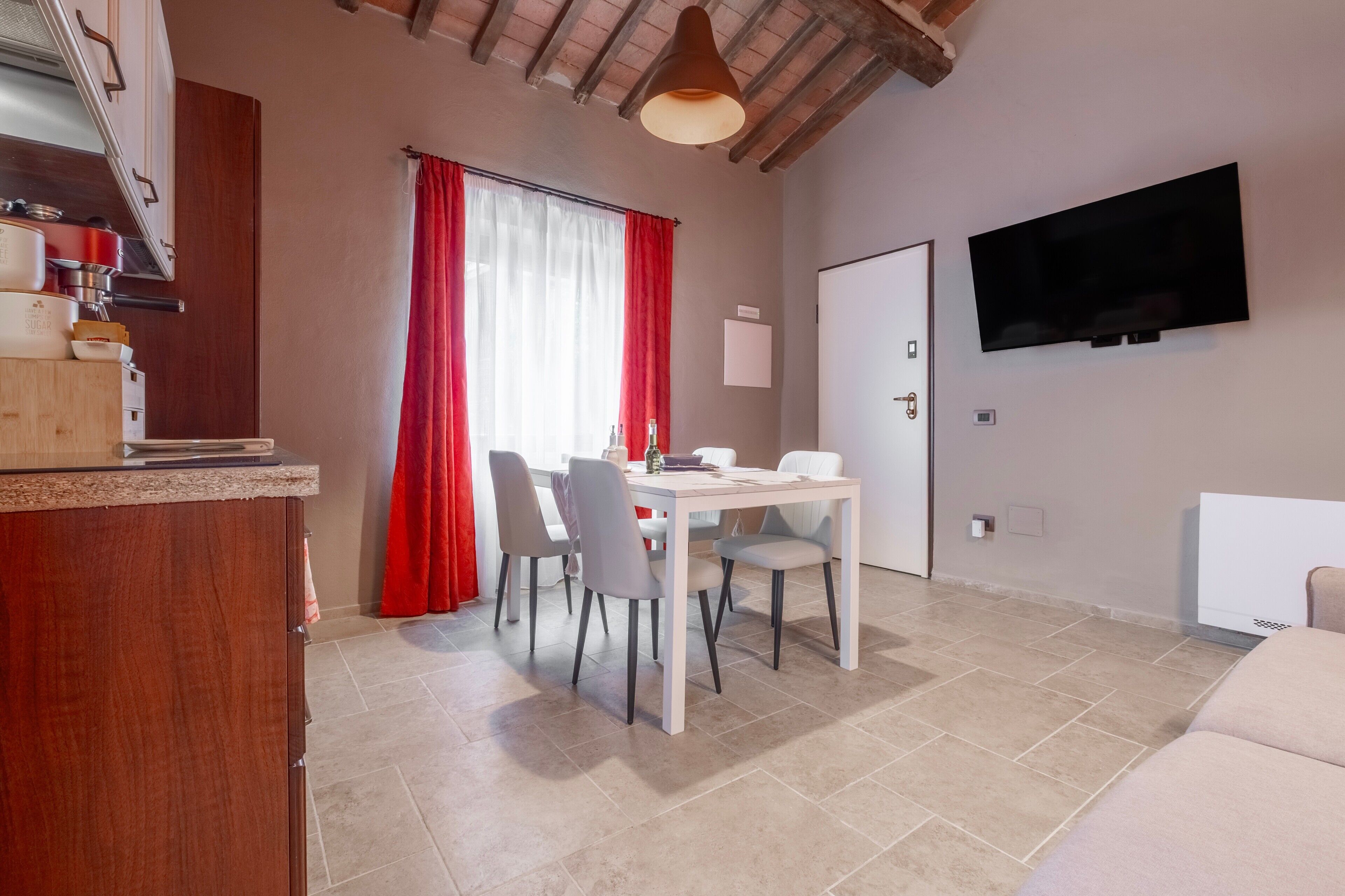 A dining area with a table and chairs, a kitchen with cabinets and a countertop, a television mounted on the wall, and a door.