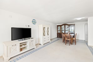 A living room with a flat-screen TV, a white cabinet, a dining table with chairs, and a kitchen area with a refrigerator. - Apartment 'Giagiumar' with Sea View, Private Terrace and Air Conditioning (Torre dei Corsari)