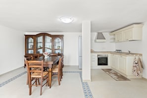 A dining area with a wooden table and chairs, a glass cabinet, and a kitchen with white cabinets and a stove. - Apartment 'Giagiumar' with Sea View, Private Terrace and Air Conditioning (Torre dei Corsari)