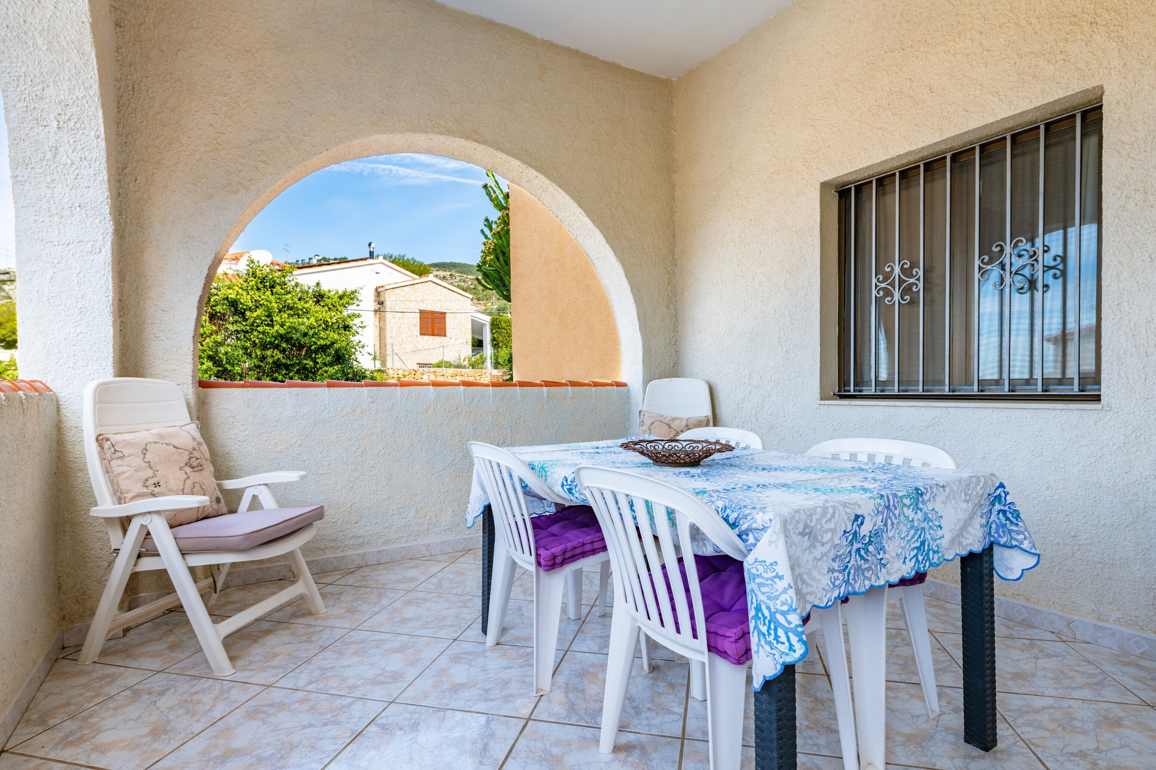 A balcony with a table, chairs, and a window with decorative bars.