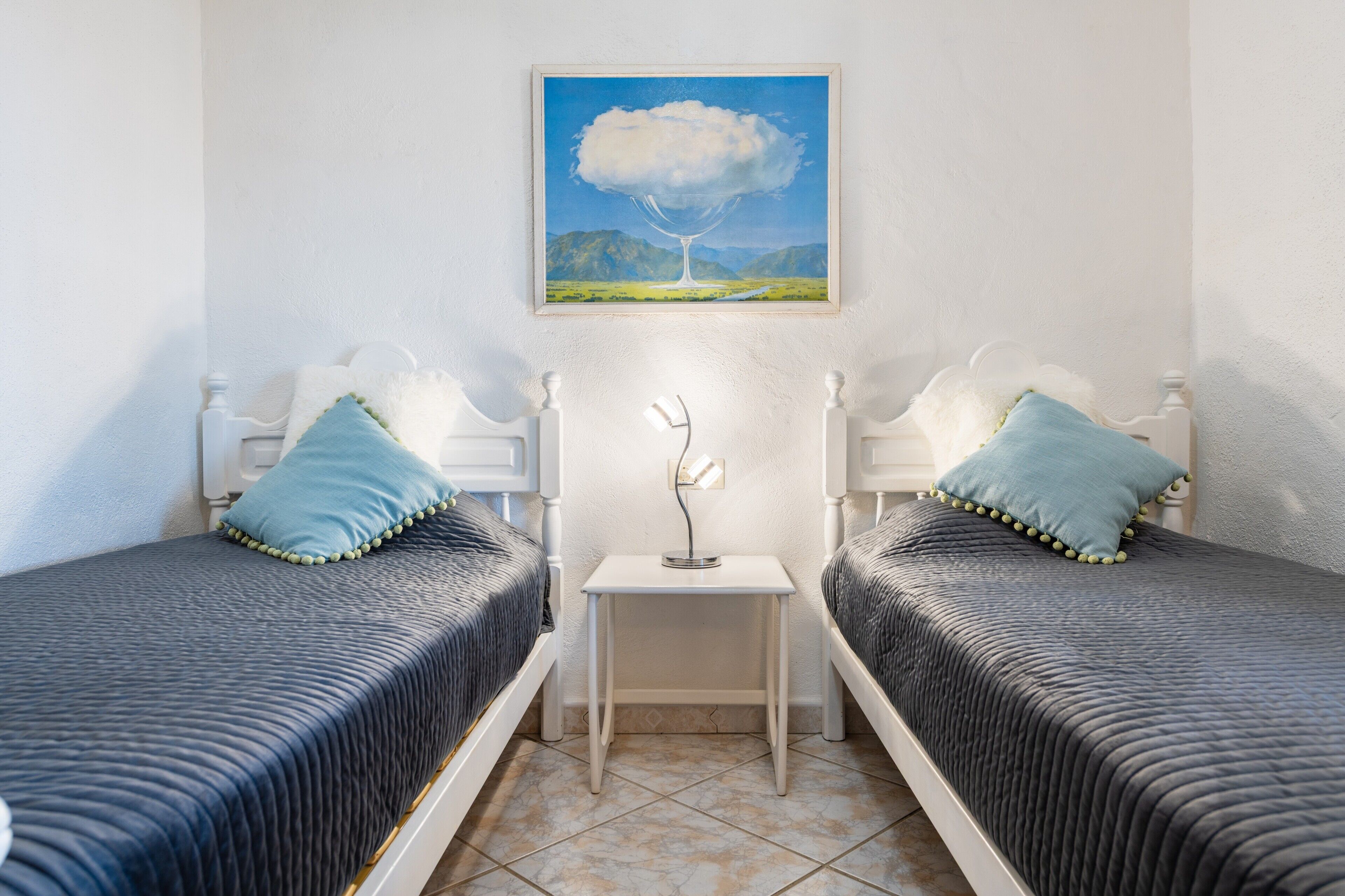 Una habitación con dos camas, una mesita peque ña y un cuadro en la pared.
