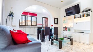 Una sala moderna con un sofá, una mesa de centro de vidrio y un televisor montado en la pared.