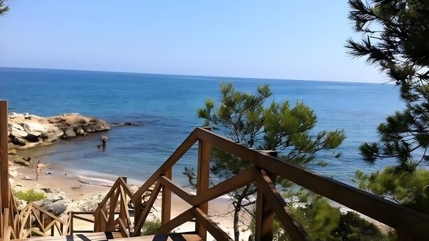 Una terraza de madera que da a una playa con agua azul cristalina y costa rocosa.