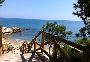 A wooden deck leading to a beach with clear blue water and rocky shoreline.