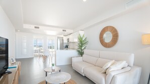Un salón moderno con un sofá blanco, un espejo redondo, una mesita con un tapete tejido y un televisor sobre un mueble de madera.