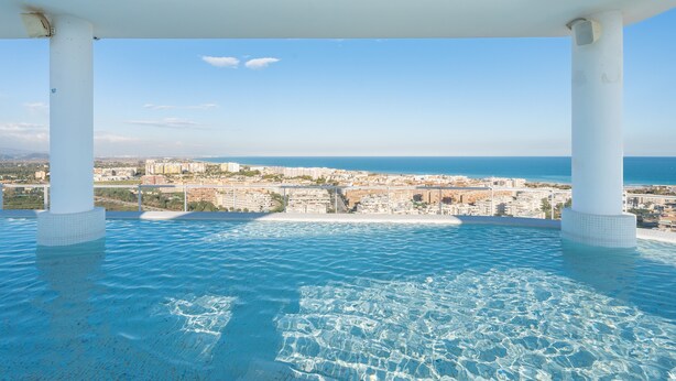 Una piscina infinita con vistas a la ciudad, pilares blancos y agua azul cristalina.