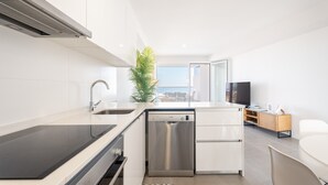Cocina moderna con lavavajillas, fregadero y estufa. Hay una planta, un televisor y vistas a la ciudad.