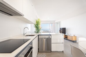 Cozinha moderna com máquina de lavar louça, pia e fogão. Há uma planta, uma televisão e vista para a cidade.