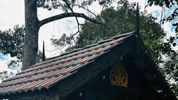 A wooden gazebo with a tiled roof, a bench, and a small table.