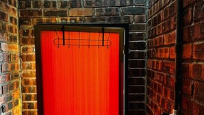 A red door with a metal handle, a brick wall, and a metal pipe on the right.