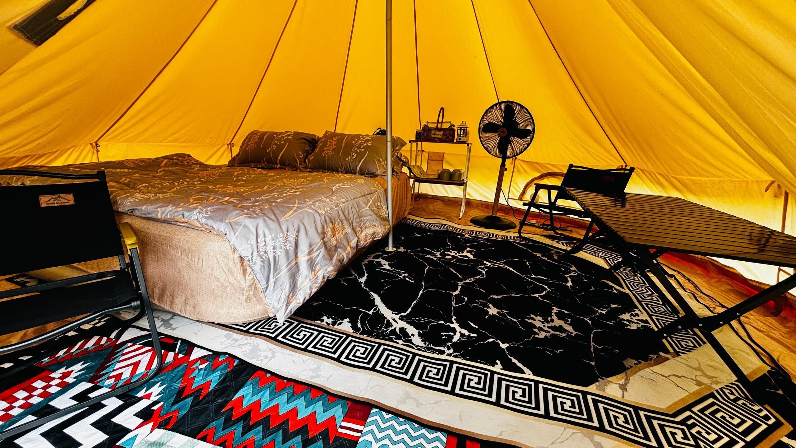 A tent with a bed, a fan, and a table.