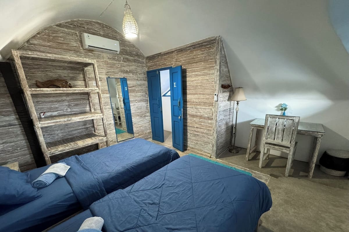A bedroom with two beds, a desk, a chair, a lamp, and a wardrobe.