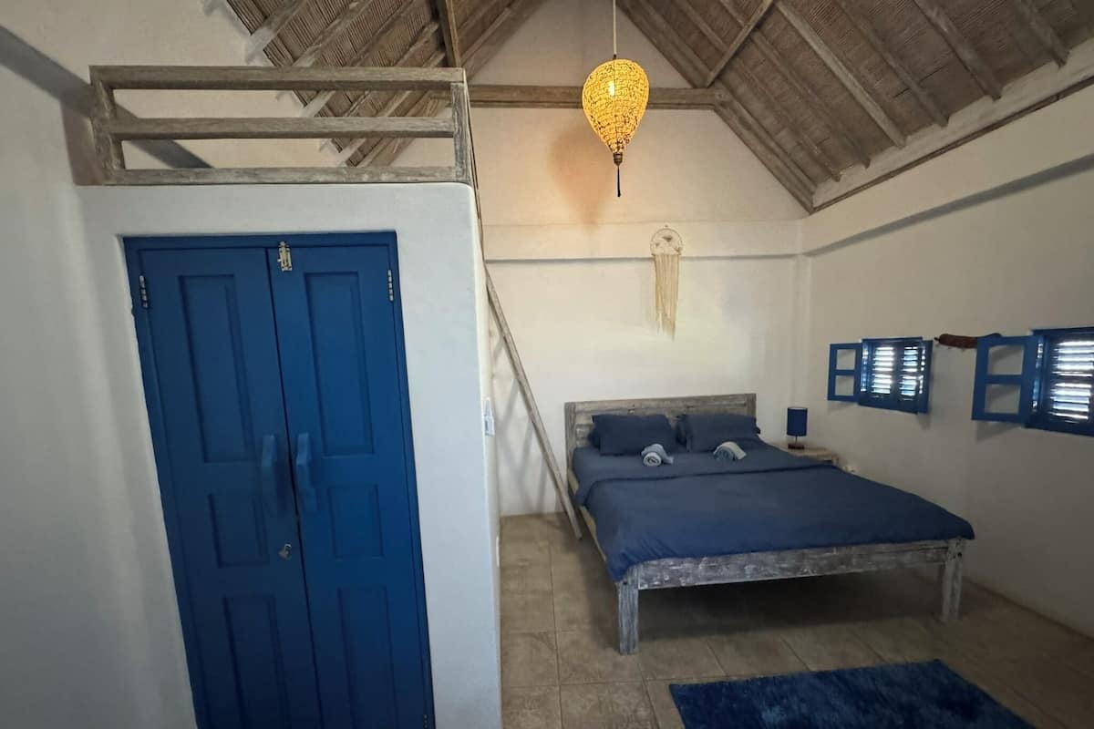 A bedroom with a blue door, a bed with a wooden headboard, a hanging light fixture, and a blue rug.