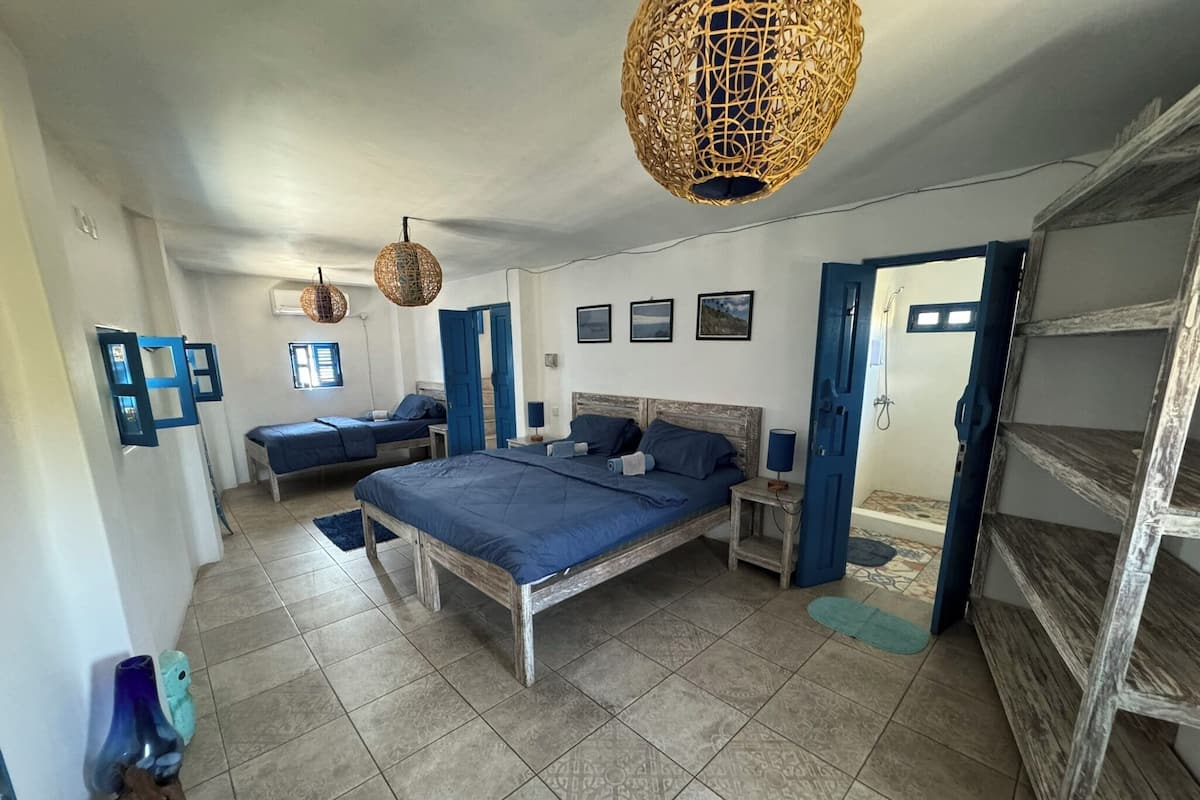 A bedroom with a large bed, two smaller beds, a wardrobe, and a bathroom visible through an open door.