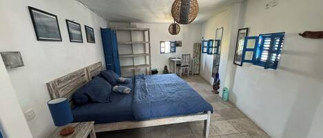 A bedroom with a bed, a small wooden table, a blue rug, and a hanging light fixture.