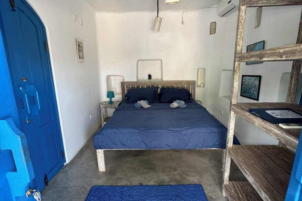 A bedroom with a bed, a blue rug, a wooden shelf, and a blue door.