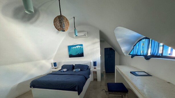 A bedroom with a bed, bedside tables, a small stool, a hanging light fixture, a painting, and a window with curtains. - Bali Bio Villas (Ungasan)