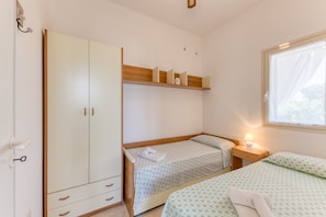 Un dormitorio con un armario, dos camas, una mesita de noche y una ventana.